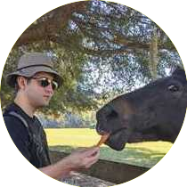 Picture of Daniel Shuster (left) feeding a carrot to a horse (right)